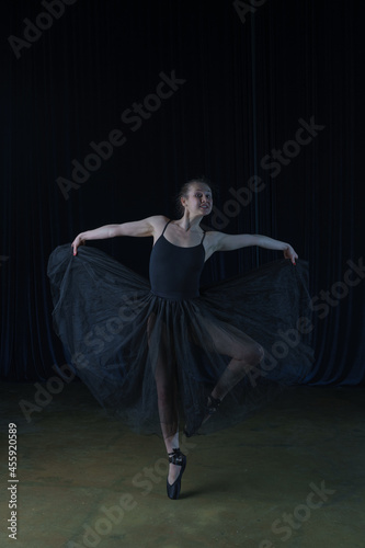 A ballerina in a black ballet costume rehearses on stage.