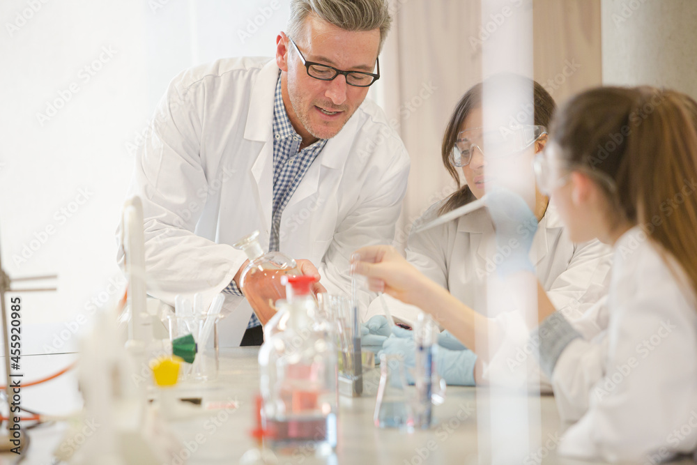 Male teacher and girl students conducting scientific experiment in laboratory classroom Male teacher and girl students conducting scientific experiment in laboratory classroom