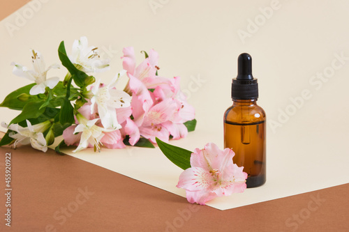 Amber glass bottle on a neutral background with a lily flowers. copy space. Cosmetic, skin care concept
