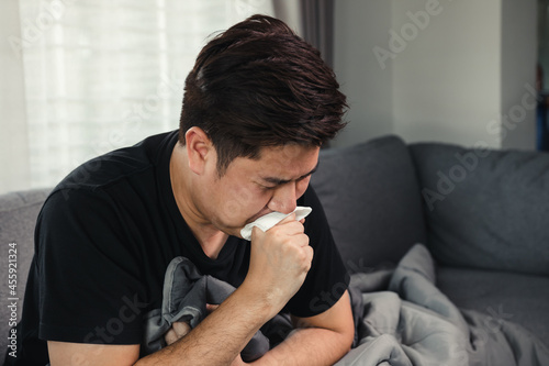 Asian people are sick or ill with bronchitis while coughing by covering their mouth with tissue paper when he sit on the sofa at home.