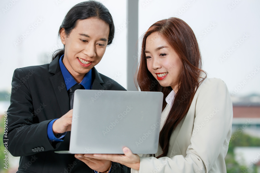 Asian young happy successful long ponytail hair businessman and confident businesswoman colleague stand smiling holding laptop computer together planning discuss about work online in company office Asian young happy successful long ponytail hair businessman and confident businesswoman colleague stand smiling holding laptop computer together planning discuss about work online in company office