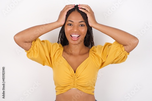 Cheerful overjoyed Young african american woman with braids over white wall reacts rising hands over head after receiving great news.
