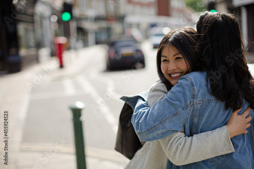 Smiling affectionate female friends hugging on sunny urban street