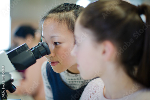 Girl students using microscope, conducting scientific experiment in laboratory classroom
