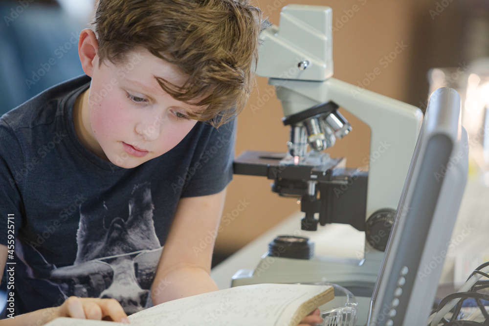 Boy student conducting scientific experiment at microscope and computer in laboratory classroom Boy student conducting scientific experiment at microscope and computer in laboratory classroom