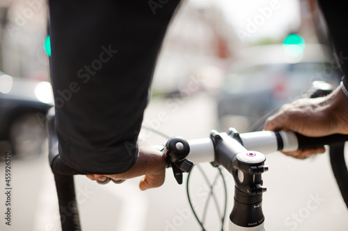 Hands on man on bicycle handlebars, commuting on sunny urban street © KOTO