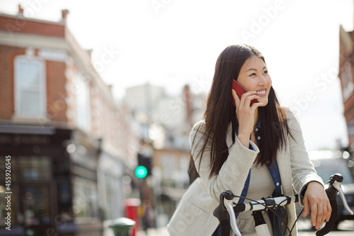 Smiling young woman commuting on bicycle, talking on cell phone on sunny urban street © KOTO