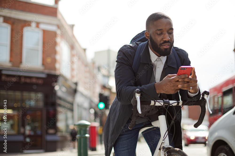 Young businessman commuting with bicycle, texting with cell phone on sunny urban street Young businessman commuting with bicycle, texting with cell phone on sunny urban street