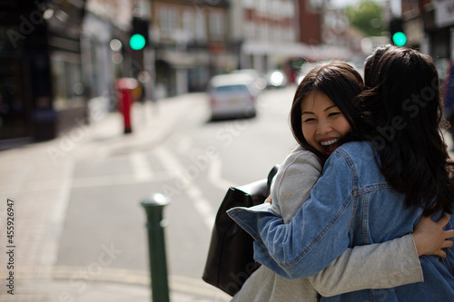 Smiling affectionate female friends hugging on sunny urban street