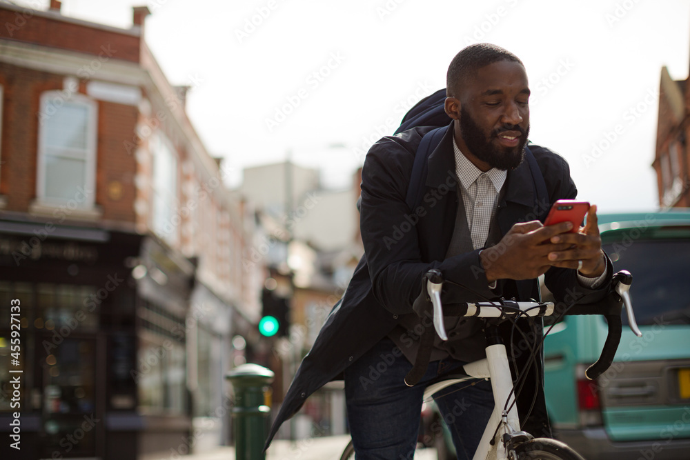 Young businessman commuting with bicycle, texting with cell phone on sunny urban street