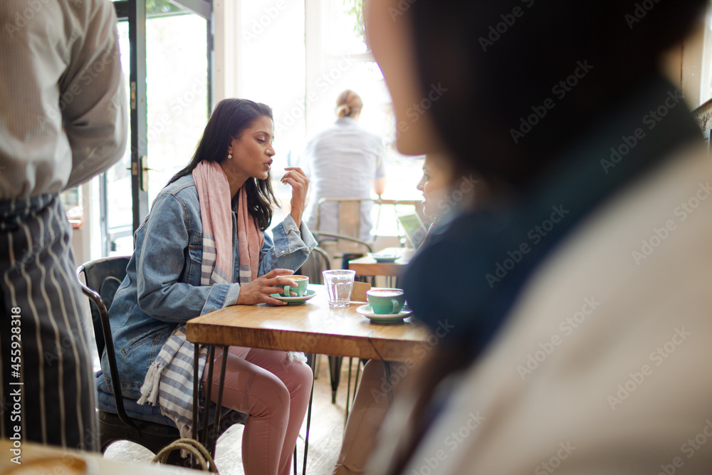 Young women friends talking and drinking cappuccinos at cafe table Young women friends talking and drinking cappuccinos at cafe table