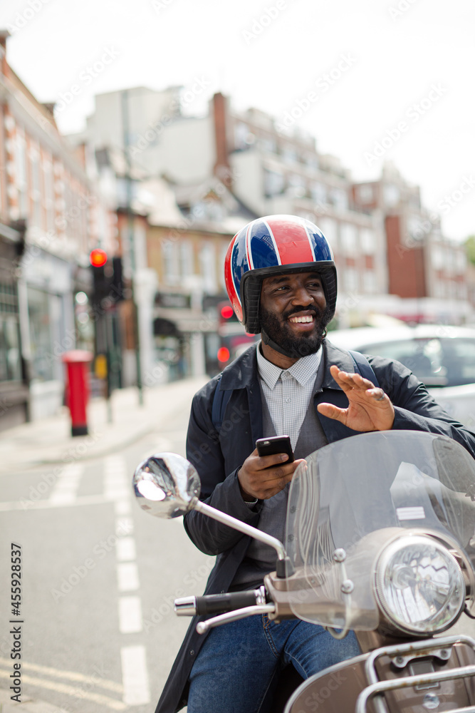 Smiling young businessman in helmet on motor scooter texting with cell phone on urban street Smiling young businessman in helmet on motor scooter texting with cell phone on urban street