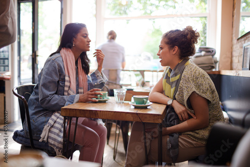 Young women friends talking and drinking cappuccinos at cafe table