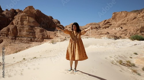 Young traveler standing in sunny desert dune and sifting particles fronm her hands. Pretty woman grabs a handful of dry sand and lets it fall between her fingers. photo