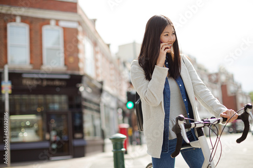 Smiling young woman commuting on bicycle, talking on cell phone on sunny urban street