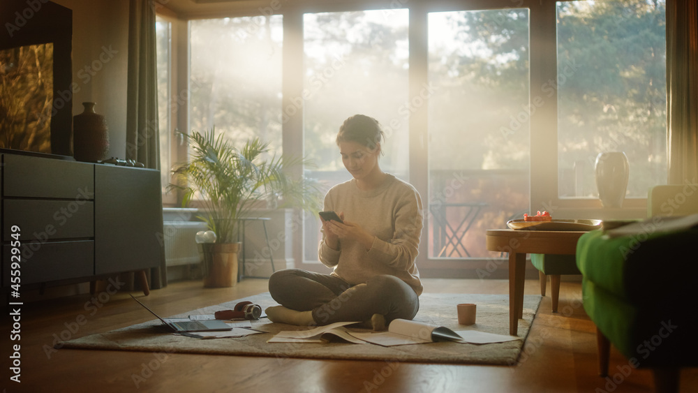 Young Woman Using Smartphone at Home, Does Remote Work. Beautiful Smiling Girl Sitting on the Floor Works with Papers, Documents, Brainstorms Creative Project with Online Research. Sunny Living Room Young Woman Using Smartphone at Home, Does Remote Work. Beautiful Smiling Girl Sitting on the Floor Works with Papers, Documents, Brainstorms Creative Project with Online Research. Sunny Living Room