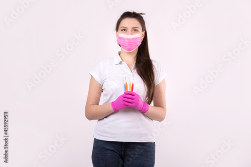 Woman dentist in pink protective mask and gloves holding tools isolated on white background.