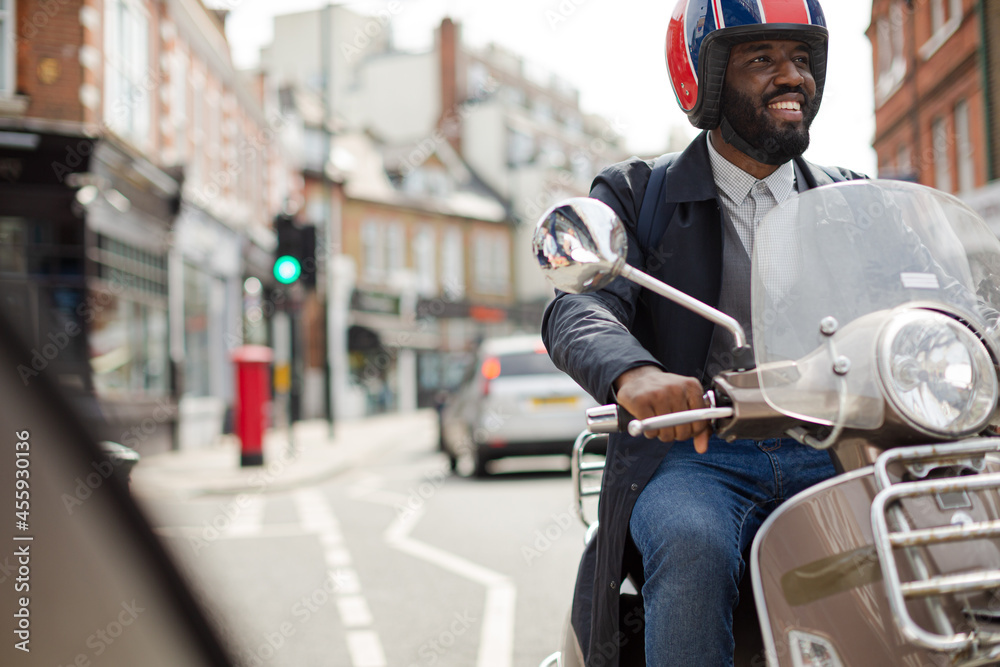 Smiling young businessman in helmet riding motor scooter on urban street Smiling young businessman in helmet riding motor scooter on urban street