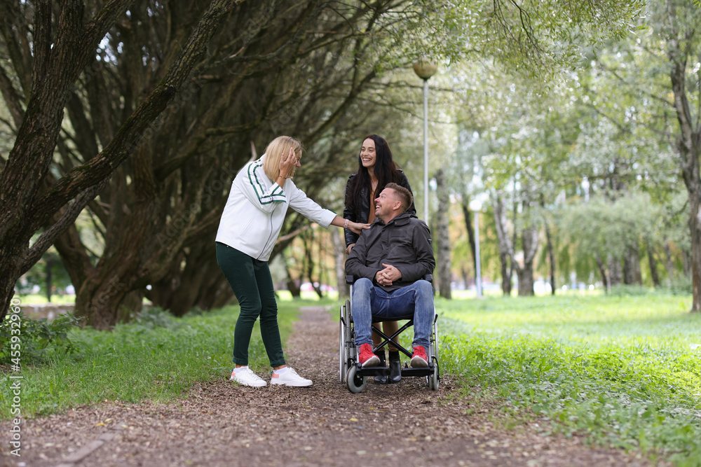 Man in wheelchair and laughing female friends walking in park