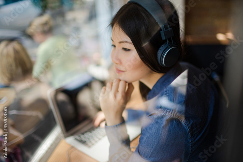Pensive young woman listening to music with headphones looking away at cafe window