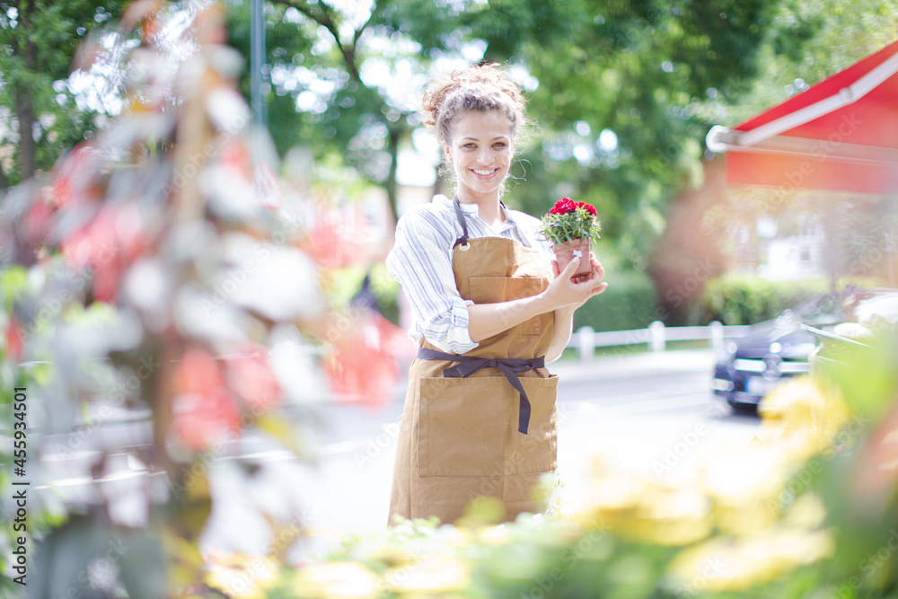 Fototapeta premium Female florist checking plants at sunny flower shop storefront