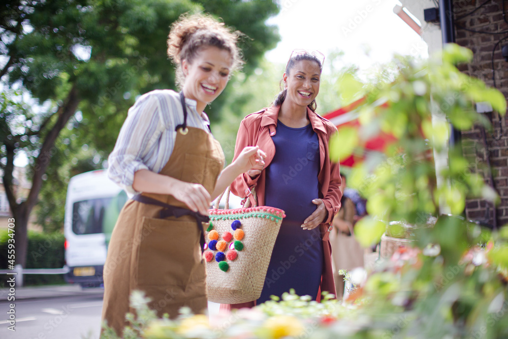 Naklejka premium Female florist helping pregnant shopper at flower shop storefront