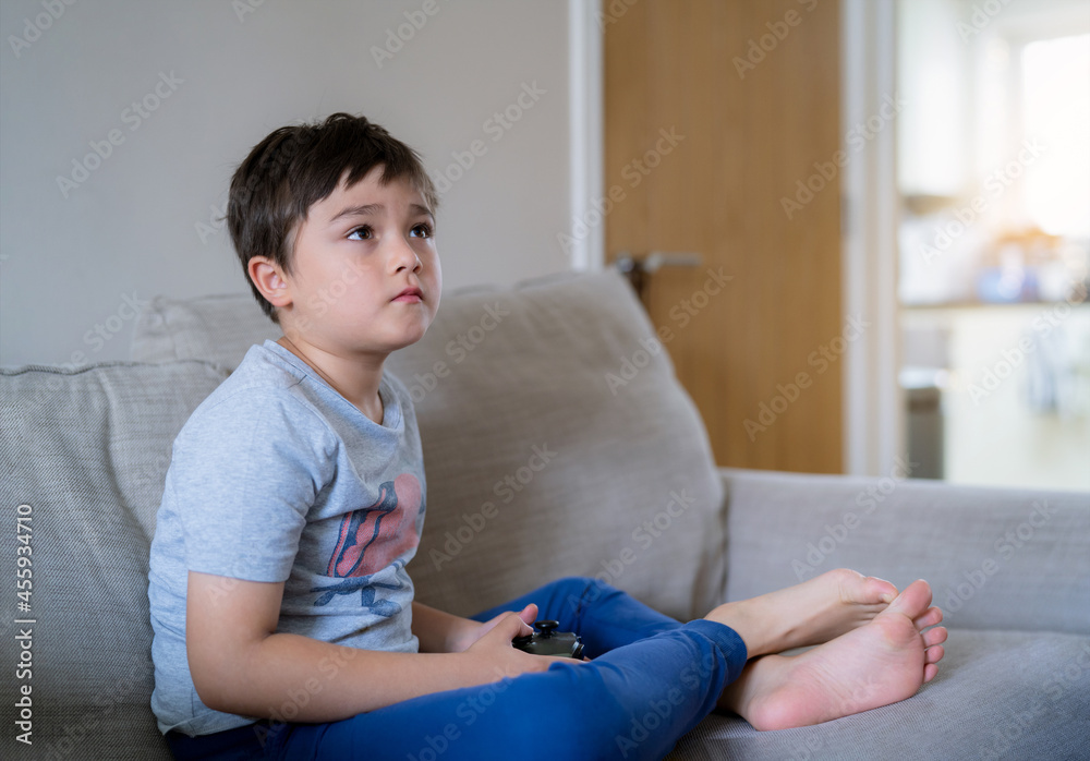 Young boy playing video games online, Candid shot Happy mixed race child  sitting on sofa holding game console. Portrait kid face looking up while  relaxing at home on weekend Stock-foto | Adobe