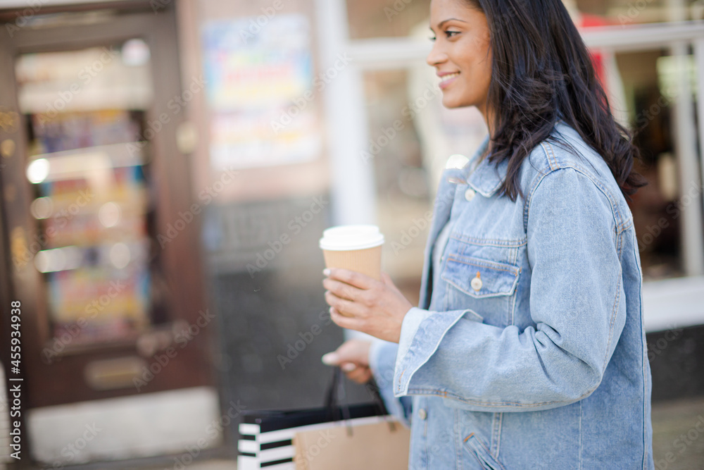 Smiling woman walking along storefront with coffee and shopping bags Smiling woman walking along storefront with coffee and shopping bags