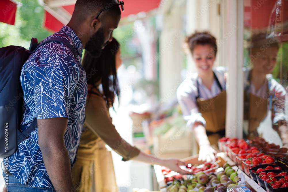 Obraz premium Female worker helping young couple shopping for fruit at market storefront