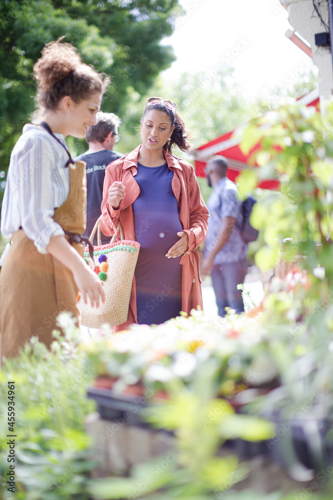 Fototapeta premium Female florist helping pregnant shopper at flower shop storefront