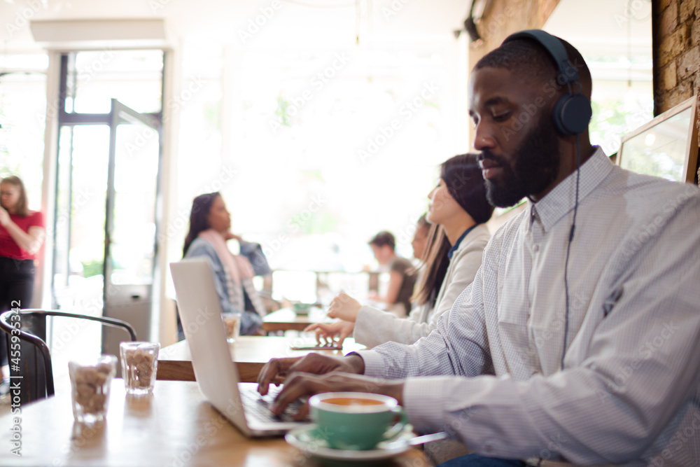 Man with headphones using laptop and drinking coffee in cafe Man with headphones using laptop and drinking coffee in cafe