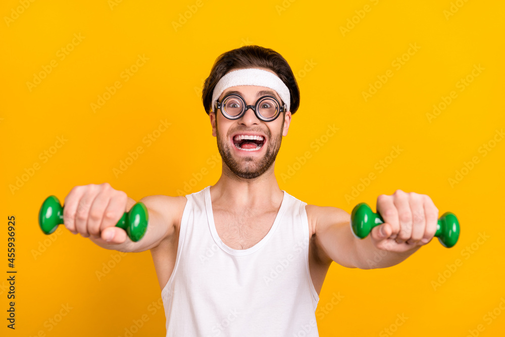 Portrait of attractive cheerful guy nerd doing work out lifting dumbbell isolated over bright yellow color background Portrait of attractive cheerful guy nerd doing work out lifting dumbbell isolated over bright yellow color background