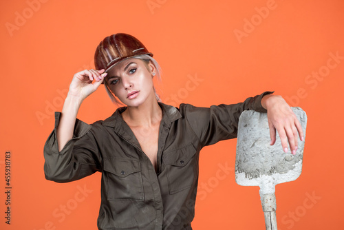 Obraz na plátně woman worker in protective helmet and boilersuit hold shovel on orange backgroun