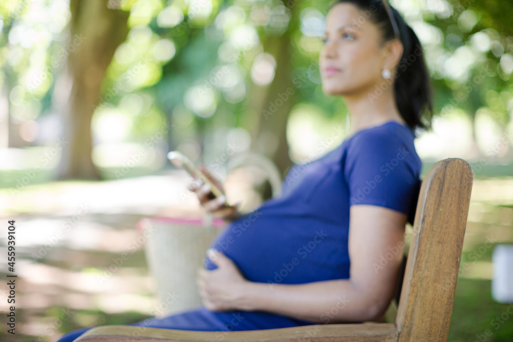 Smiling pregnant woman texting with cell phone on park bench Smiling pregnant woman texting with cell phone on park bench