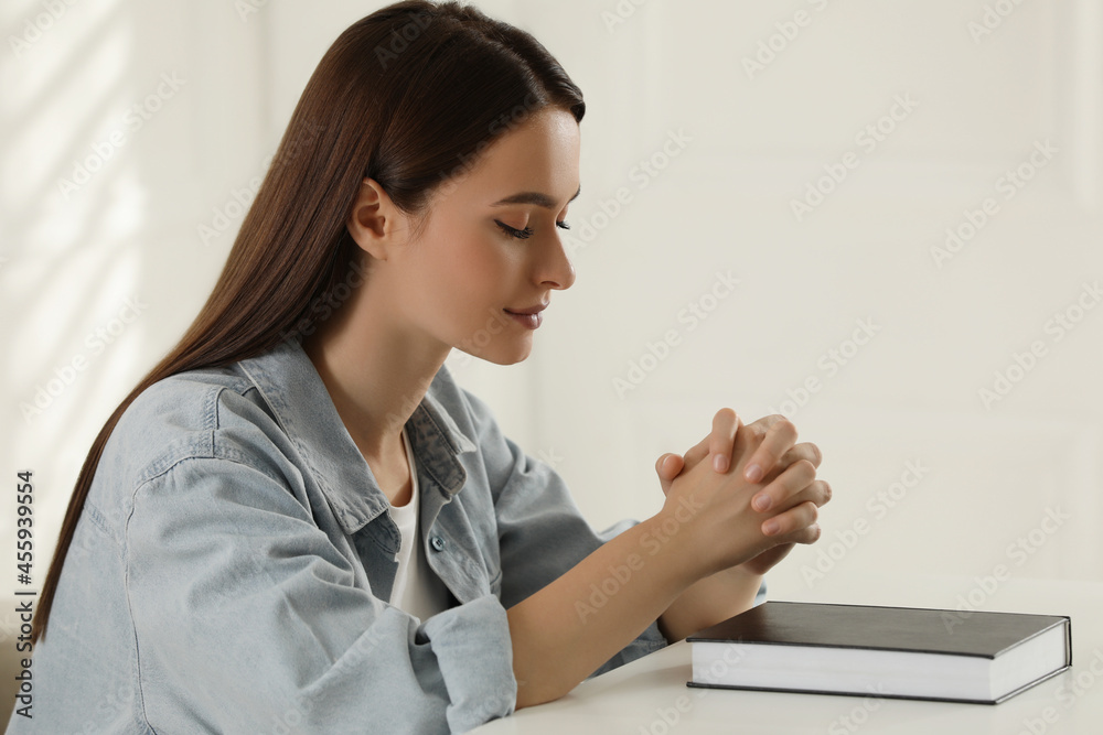 Religious young woman praying over Bible at table indoors Religious young woman praying over Bible at table indoors