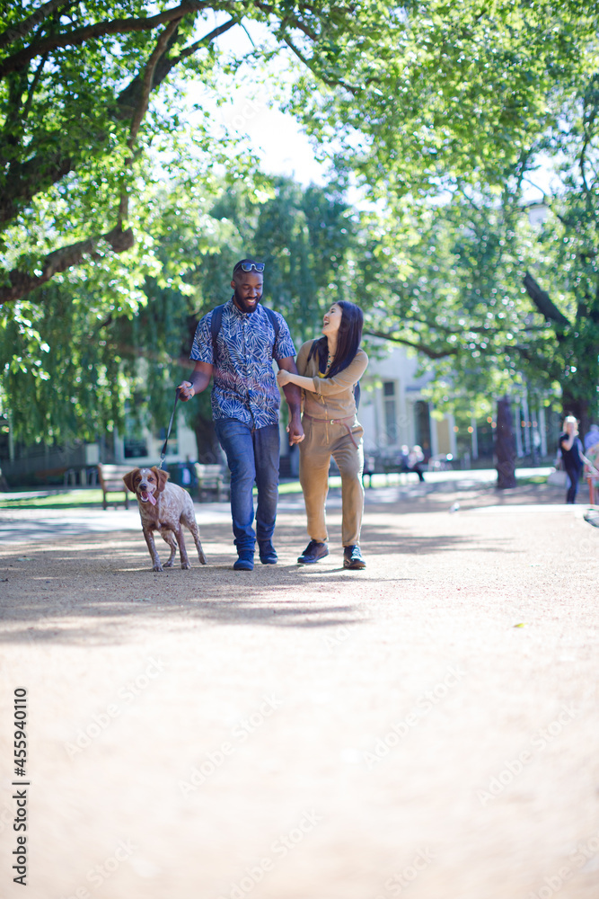 Obraz premium Happy young couple walking dog in sunny park