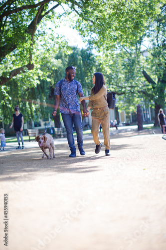 Happy young couple walking dog in sunny park