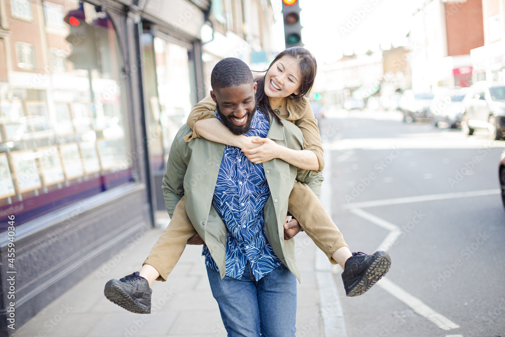 Playful young couple piggybacking on urban street