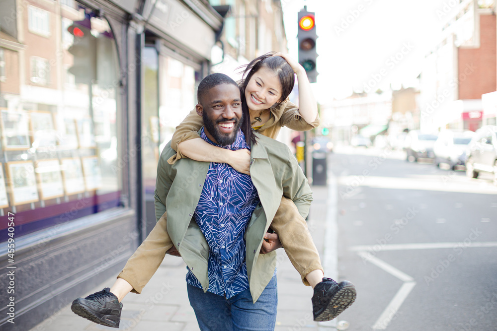 Playful young couple piggybacking on urban street Playful young couple piggybacking on urban street
