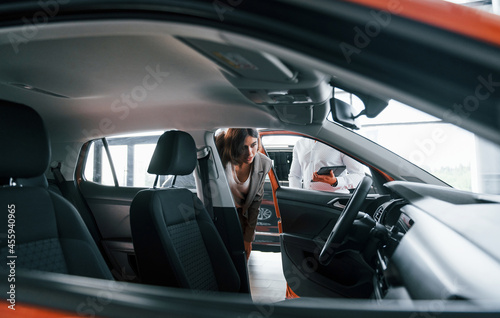 Looking at interior. Man in formal wear helping customer with choice of the automobile