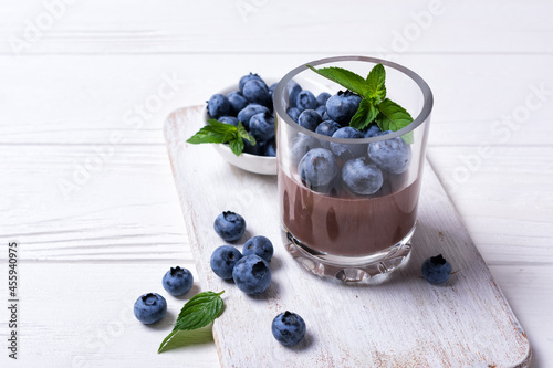 Chocolate pudding with blueberry and mint in glass on white wooden background