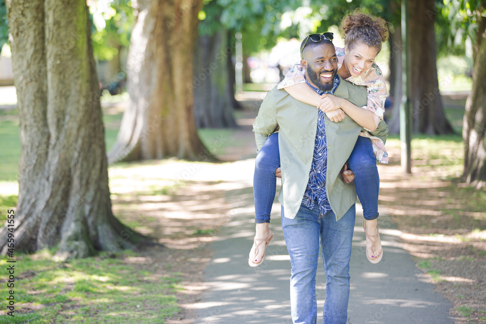 Playful young couple piggybacking in park Playful young couple piggybacking in park