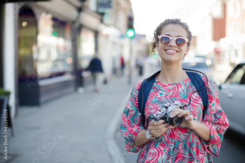 Portrait laughing, enthusiastic young female tourist in sunglasses photographing with camera on urban street