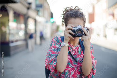 Portrait laughing, enthusiastic young female tourist in sunglasses photographing with camera on urban street