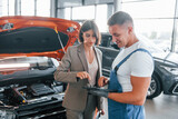 With female customer. Man repairing woman's automobile indoors. Professional service