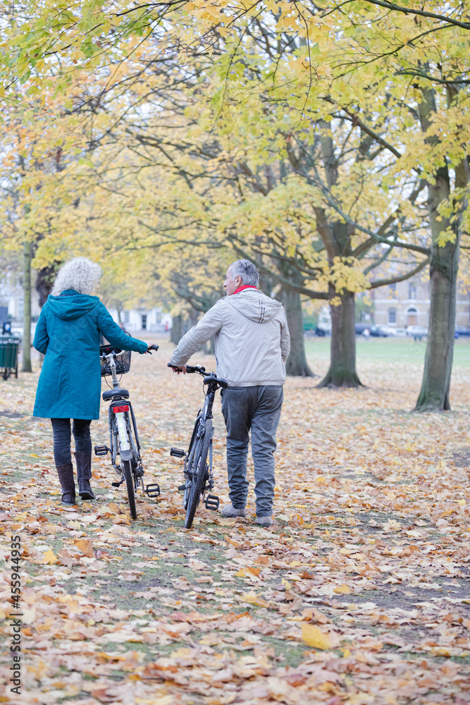 Senior couple walking bicycles among trees and leaves in autumn park Senior couple walking bicycles among trees and leaves in autumn park