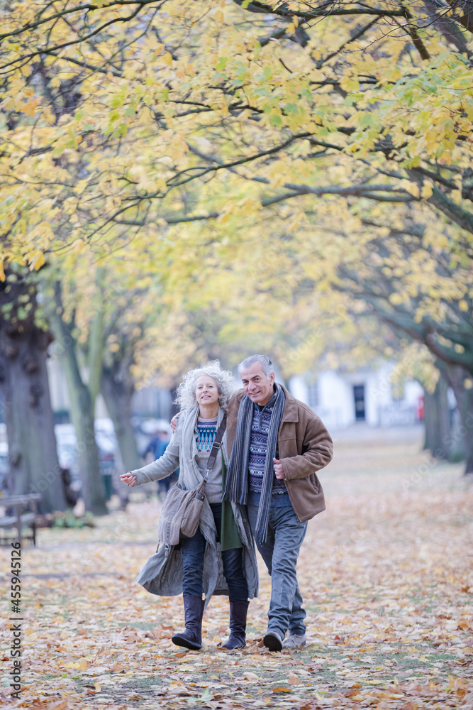 Affectionate couple hugging, walking among trees and leaves in autumn park