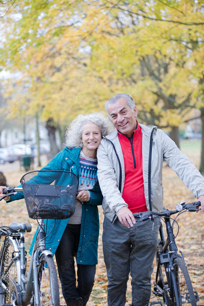 Senior couple walking bicycles among trees and leaves in autumn park