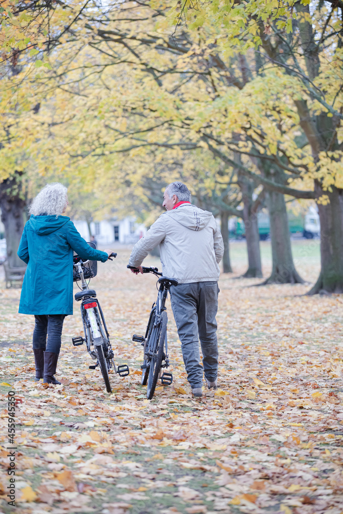 Senior couple walking bicycles among trees and leaves in autumn park Senior couple walking bicycles among trees and leaves in autumn park