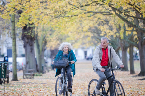 Fototapeta Naklejka Na Ścianę i Meble -  Senior couple bike riding among trees and leaves in autumn park